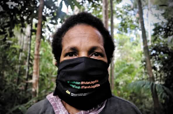 Papoea-vrouw met mondmasker met in het Indonesisch de opschrift "Bescherm het bos – het bos beschermt ons"