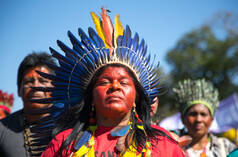 Een met een verenkroon versierde inheemse vrouw; op de achtergrond twee andere vrouwen