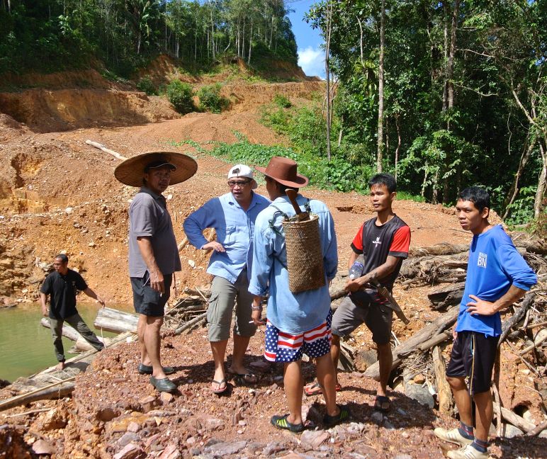 Een illegale houthakkersweg blokkeert de rivier die de Iban als verbindingsweg dient Inheemse mensen staan op een weg die houthakkers illegaal hebben aangelegd in Sarawak