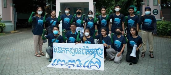 De jeugdgroep Mother Nature Cambodia bij de overhandiging van de petitie voor het ministerie van Toerisme. Op het spandoek staat: “Koh Kong Island moet een nationaal zeepark worden” (© Mother Nature Cambodia) 15 jongeren staan en knielen voor het gebouw van het ministerie van Toerisme en houden een spandoek voor de camera. Daarop staat: “Koh Kong Island moet een nationaal zeepark worden”
