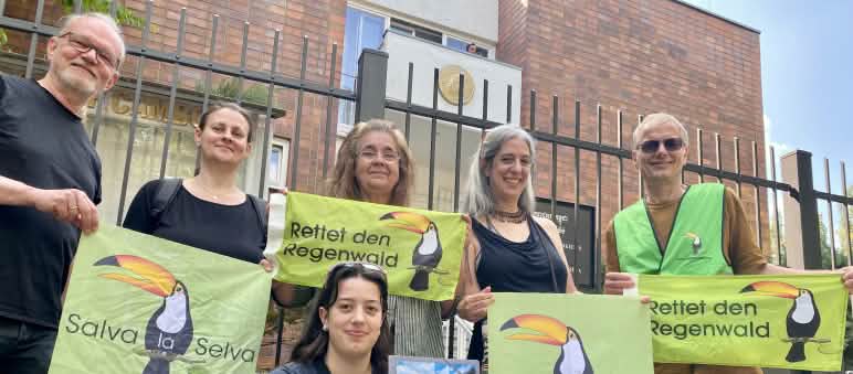 6 mensen staan voor het ambassadegebouw met een spandoek waarop staat: “Red het Regenwoud” (in het Duits en Spaans) en de toekan als symbool van de vereniging