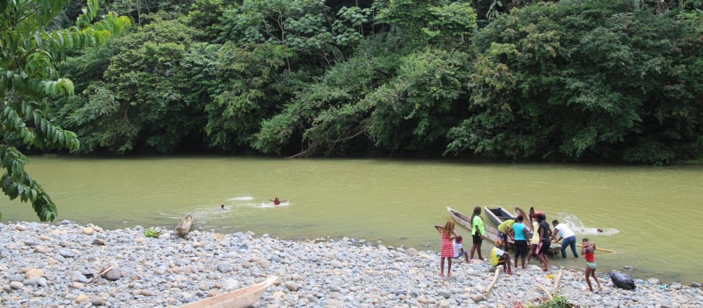 Mensen met kano's aan de oever van een rivier in het regenwoud en kinderen die in het water zwemmen