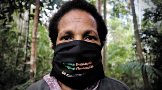 Papoea-vrouw met mondmasker met in het Indonesisch de opschrift "Bescherm het bos – het bos beschermt ons"