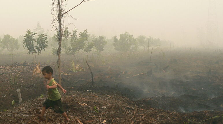 Een kindje loopt over smeulende veenbodem in Katingan, Borneo