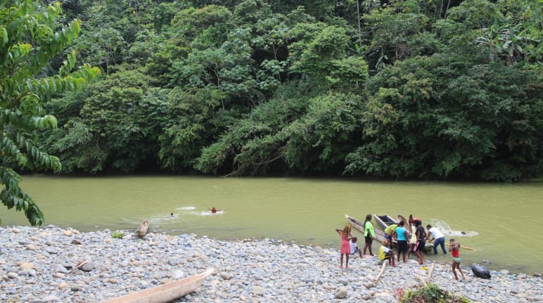 Mensen met kano's aan de oever van een rivier in het regenwoud en kinderen die in het water zwemmen