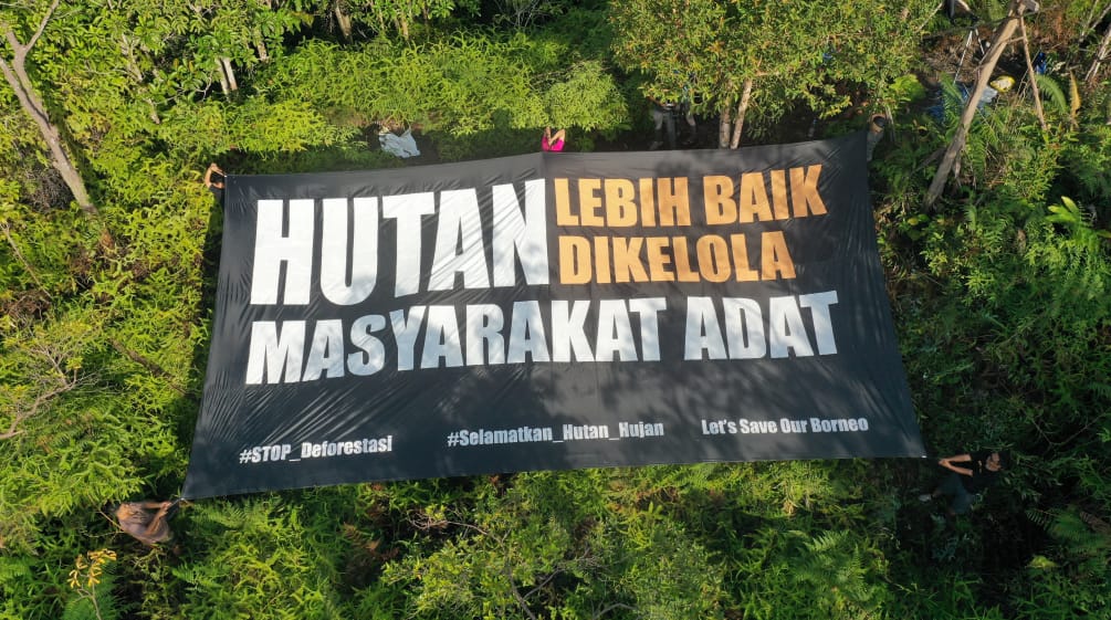 Groot spandoek met de tekst "Het bos wordt beter beschermd door de inheemse bevolking" (Nederlandse vertaling)